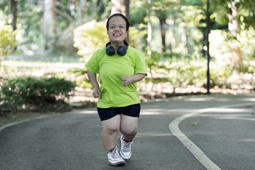 Petite Woman Jogging in Park with Headphones on a Sunny Day, Embracing Fitness and Healthy Lifestyle in a Green Natural Setting photo
