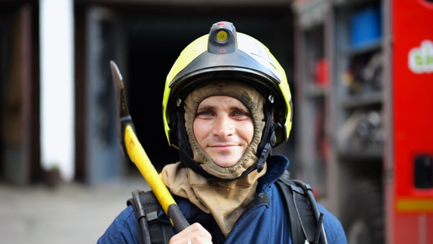 Portrait of happy male fireguard with axe standing near a fire engine. Young smiling fireman looking at camera in full equipment after fire near big red truck. Saving lives and heroic profession photo
