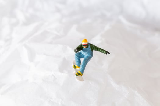 Miniature people snowboarder dressed in vibrant winter gear, carving through a snowy slope photo