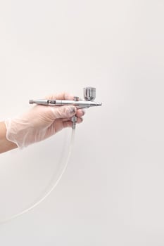 Caucasian female hand holding airbrush tool with gloves against white background. photo