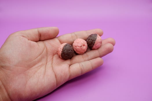 Chocolate soccer ball snack, half pink and half brown, held in hand against purple background photo