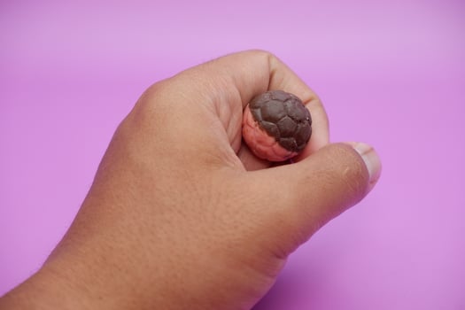 Hand holding soccer ball shaped chocolate snack, half brown and half pink, on purple photo