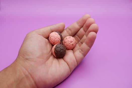 Chocolate ball snack resembling a soccer ball, half pink and brown, held in hand on purple background photo