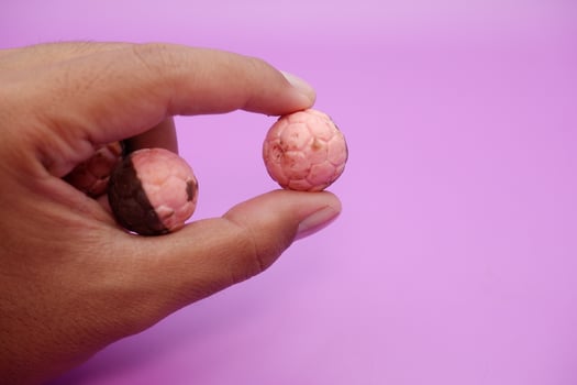 Hand holding chocolate ball snack with pink and brown halves on purple backdrop photo