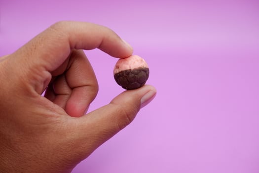 Hand holding soccer ball shaped chocolate snack, pink and brown halves, isolated on purple photo