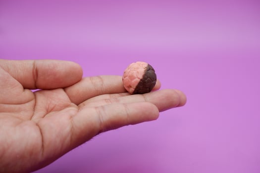 Half brown, half pink chocolate ball snack resembling a soccer ball, held in hand on purple background photo