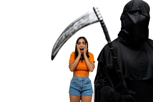 Frightened young woman threatened by grim reaper in Halloween costume holding a scythe photo