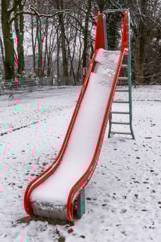 Red slide covered with snow in a playground during winter photo