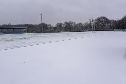 Snow covering soccer field during winter season with bleachers and cloudy sky photo