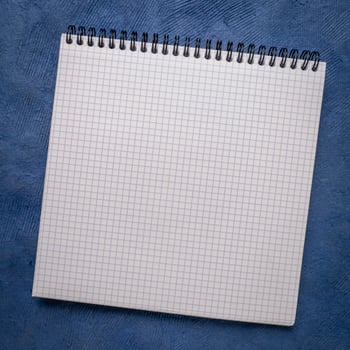 blank spiral notebook with grid paper on textured art paper photo