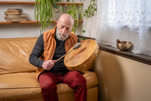 senior man is playing native American style, shaman drum with a beater at home, lifestyle and hobby concept photo