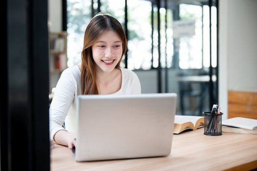 A smiling, happy Asian female college student working on her project on her laptop in a coffee shop. photo