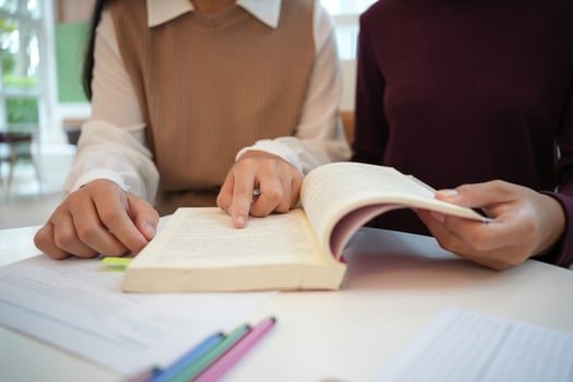 Learning with friends two people sitting at a table with a book and pencils photo