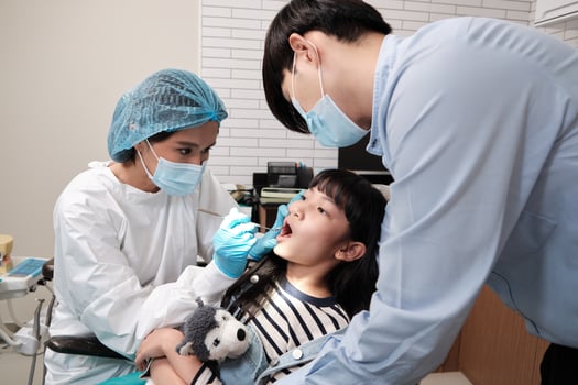 Asian female pediatric dentist examines a girl's teeth in dental clinic and takes care and encourages of father, mouth oral hygiene, and professional orthodontic healthcare work in a kid hospital. photo