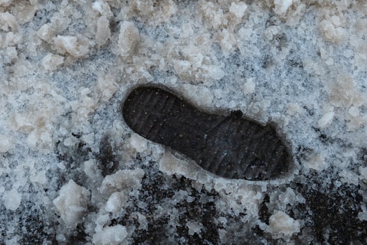 Snow-covered ground shows a single shoeprint left behind in a cold winter landscape photo