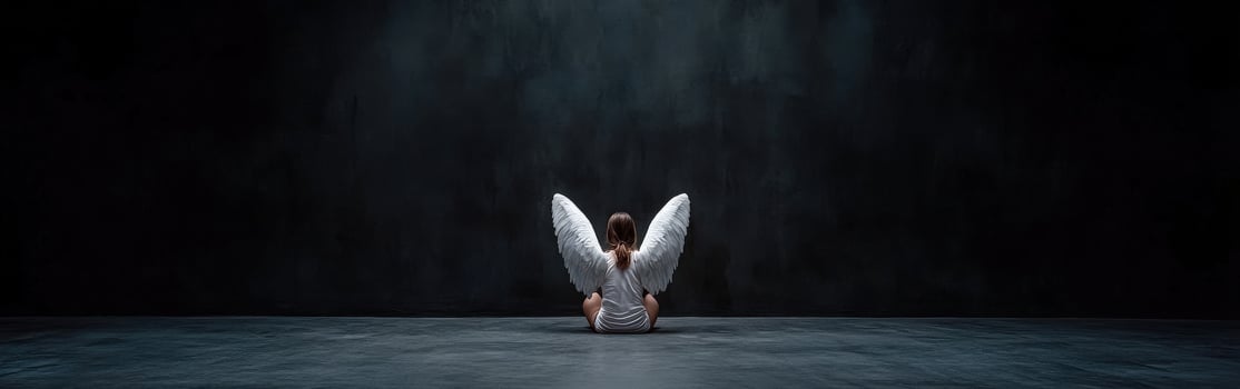 Child with angel wings sitting on a dark stage during a performance photo