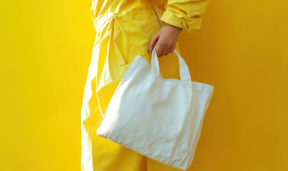 Woman wearing yellow clothes holding a white tote bag mockup, promoting reusable bags and eco friendly shopping habits photo