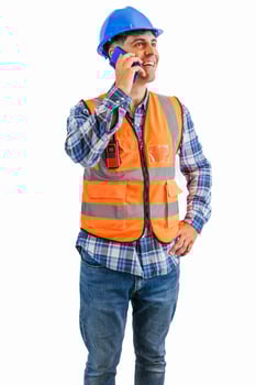 vertical Smiling construction worker making call with his smartphone wearing orange vest and helmet photo