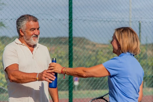 Close-up of elderly tennis couple sharing water bottle during match on hot day photo