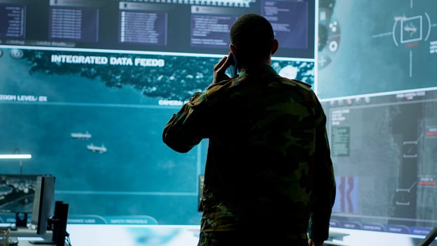 Military man answers phone call in a mission control center, working with advanced technology and satellite imagery to track potential threats and real time data. Intelligence activities. Camera A. photo