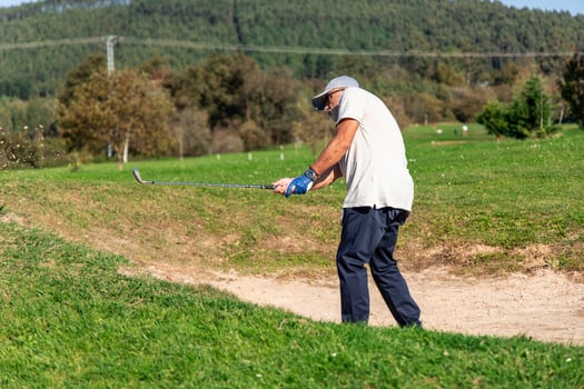 elderly golfer skillfully hitting ball out of sand bunker photo