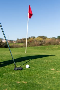 Close-up of a putter ready to strike the golf ball towards with the flag stick in the background photo
