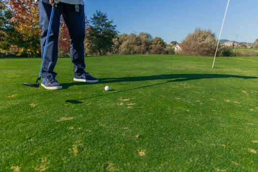 unrecognizable elderly golfer hitting the ball with the putter towards the hole on the green photo
