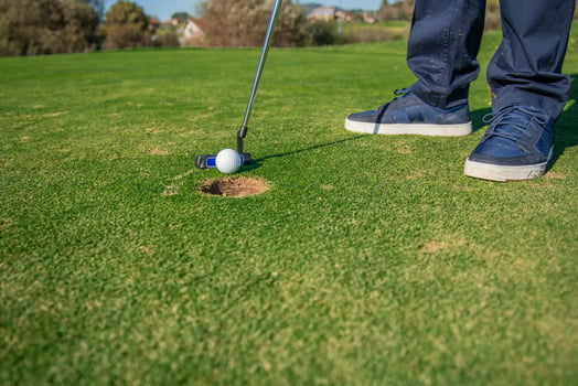 copyspace Close-up of golfer's feet striking the ball with a putter toward the hole on the green photo