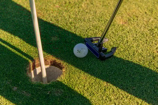 Close-up of putter hitting ball near hole on the green photo