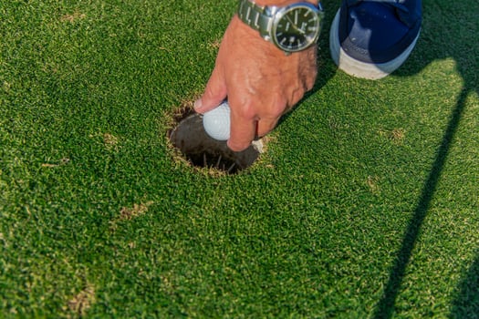 closeup senior golfer's hand with wristwatch retrieving golf ball from hole on the green photo