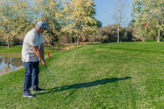 copyspace elderly golfer hitting ball toward green flag near lake photo