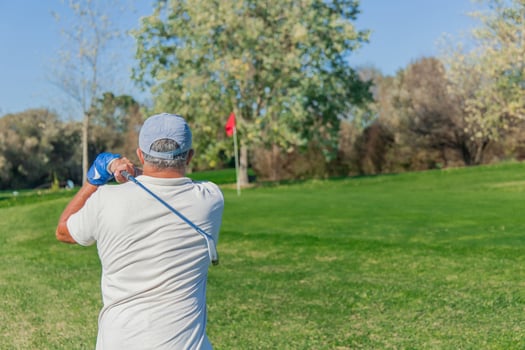 copyspace senior golfer seen from behind with club raised after hitting ball toward green flag photo