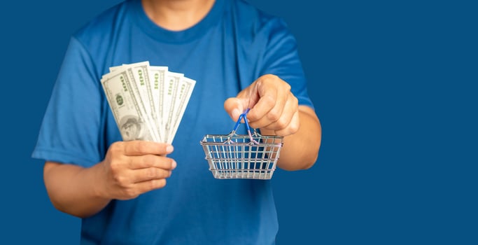 Man in a blue casual holding a mini shopping cart and US banknotes while standing on a blue blackground photo