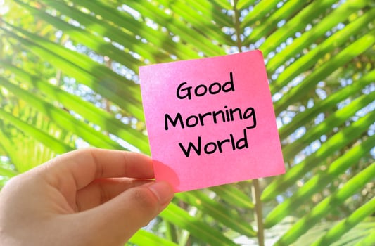 Hand holding a pink note that says GOOD MORNING WORLD with a background of trees and forest in the morning, the concept of welcoming the morning with natural views photo