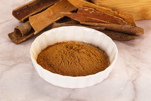 A bowl of cinnamon powder and sticks on a marble surface photo