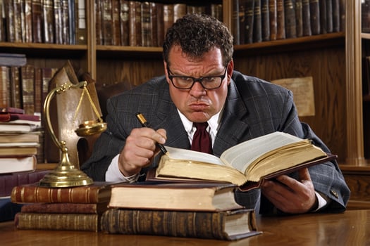 A man in a suit and tie sitting at a desk with a book and a scale photo