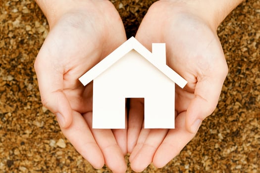 Hands holding a house paper model on brown background photo
