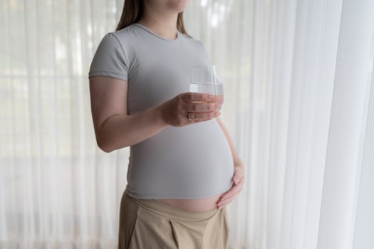 Pregnancy and Hydration. Pregnant woman holding a glass of mineral water, drinking water, touching belly. Closeup photo