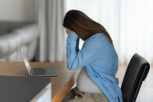 Unhappy pregnant woman with headache sitting on chair at desk in home office photo