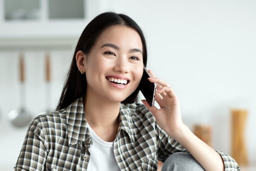 Young asian lady having healthy breakfast and talking on phone, smiling and looking at copy space. Cheerful woman sitting at kitchen, eating oatmeal and chatting with girlfriend or lover photo