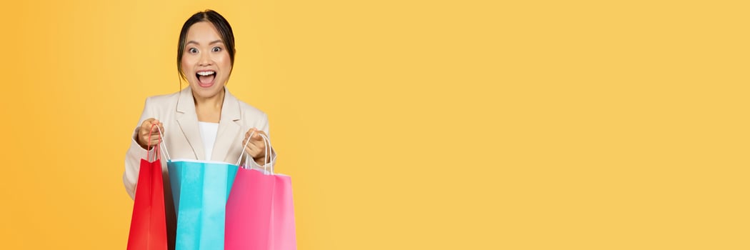 Surprised glad young japanese lady shopaholic open colorful bags, with purchases enjoy shopping, isolated on orange studio background. Huge sale, lifestyle and new fashion photo