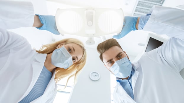 Two dentists caucasian man and woman in face masks and rubber gloves doing treatment, turning on lamp, shot from dental chair. Modern stomatology, high class dental clinic concept photo