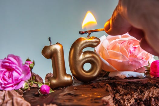 Closeup of a womans hand lighting golden 16 candles on a chocolate birthday cake decorated with pink and peach roses for a sweet sixteen celebration. photo