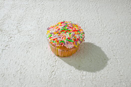 a cupcake with sprinkles on top of a white surface background photo