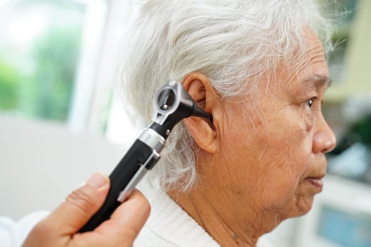 Otolaryngologist or ENT physician doctor examining senior patient ear with otoscope, hearing loss photo