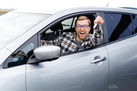 Excited young man showing a car key, sitting inside his new vehicle. photo