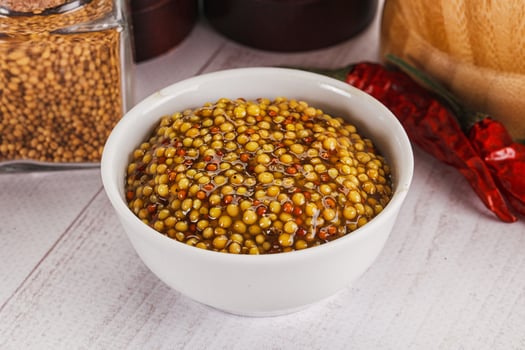 A bowl of mustard seeds and a jar of chili peppers photo
