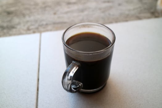 a glass of black coffee in a glass cup photographed from the side, during the day photo