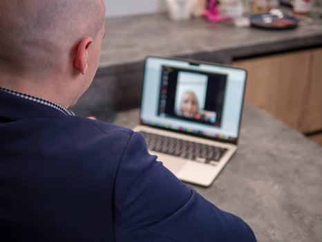 Businessman working from home using laptop for conference with female colleague, discussing business strategies in modern kitchen. Laptop enables seamless remote communication photo