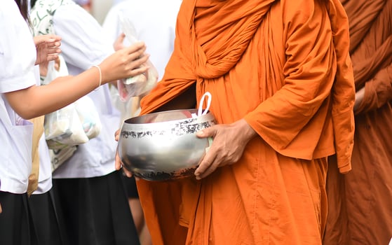 A monk is holding a silver bowl and a woman is giving him money photo